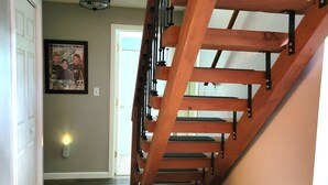 Una escalera de madera con un banco al pie, un pasillo con suelo estampado y un cuadro en la pared.