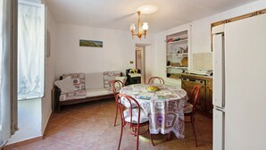 Un espace repas comprenant une table, des chaises, un lustre, un canapé et un coin cuisine avec des placards et un réfrigérateur.