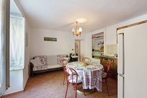Un espace repas comprenant une table, des chaises, un lustre, un canapé et un coin cuisine avec des placards et un réfrigérateur.