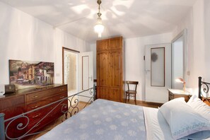 Une chambre à coucher avec un lit, une armoire en bois, un bureau avec une chaise, un tableau au mur et un luminaire au plafond.