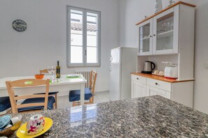 A kitchen with a granite countertop, white cabinets, a window, and a clock on the wall.