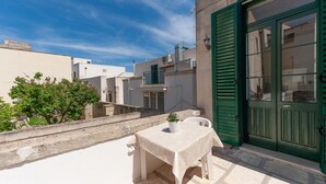 A balcony with a table and chair, a potted plant, and a green door. - "Casa in Via Seminario" Apartment with Balcony and Wi-Fi (Otranto)