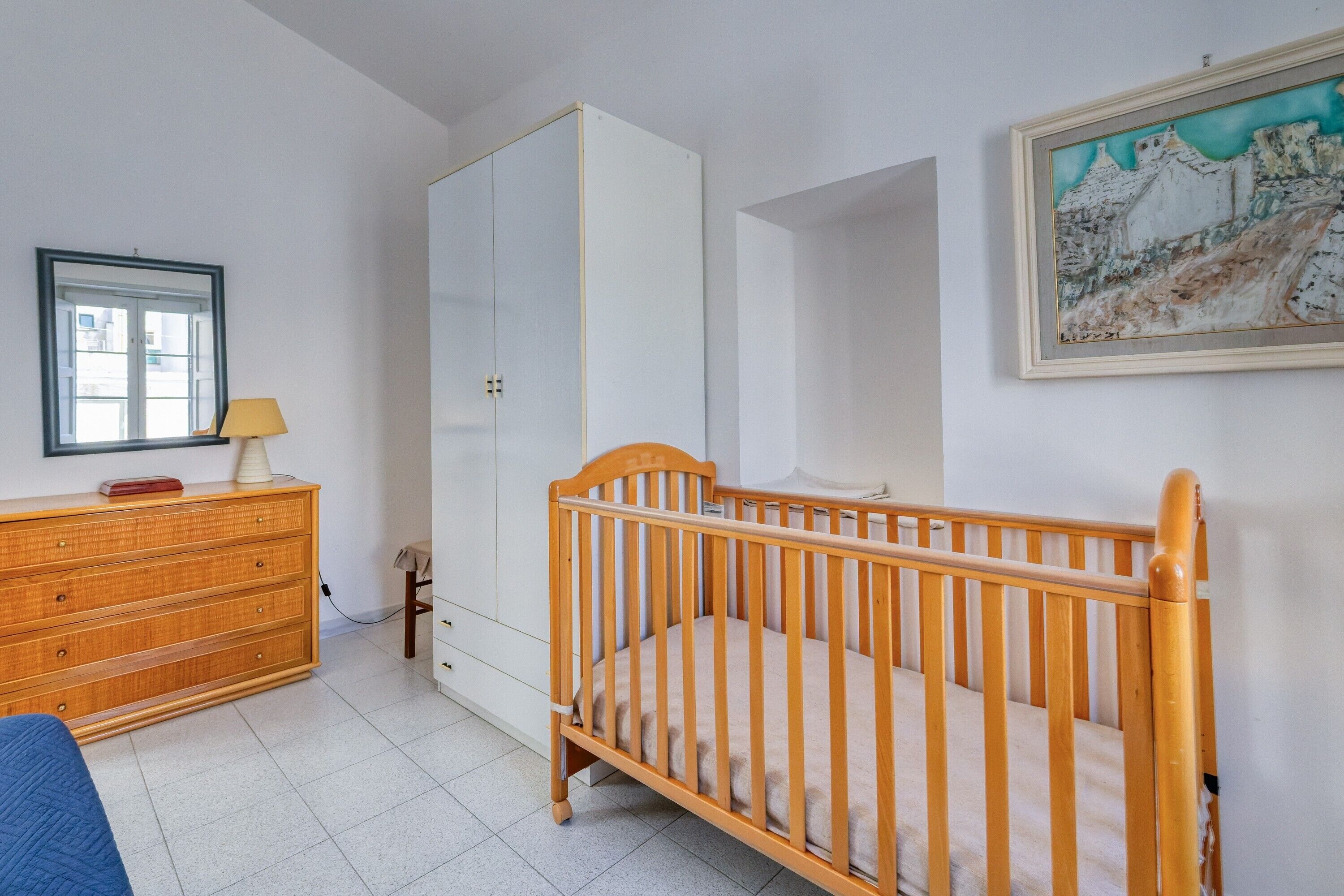 A bedroom with a crib, dresser, and a painting on the wall.