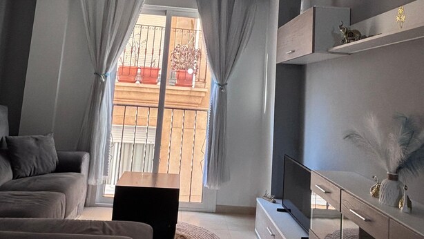 En moderne stue med sofa, tv og balkonudsigt.