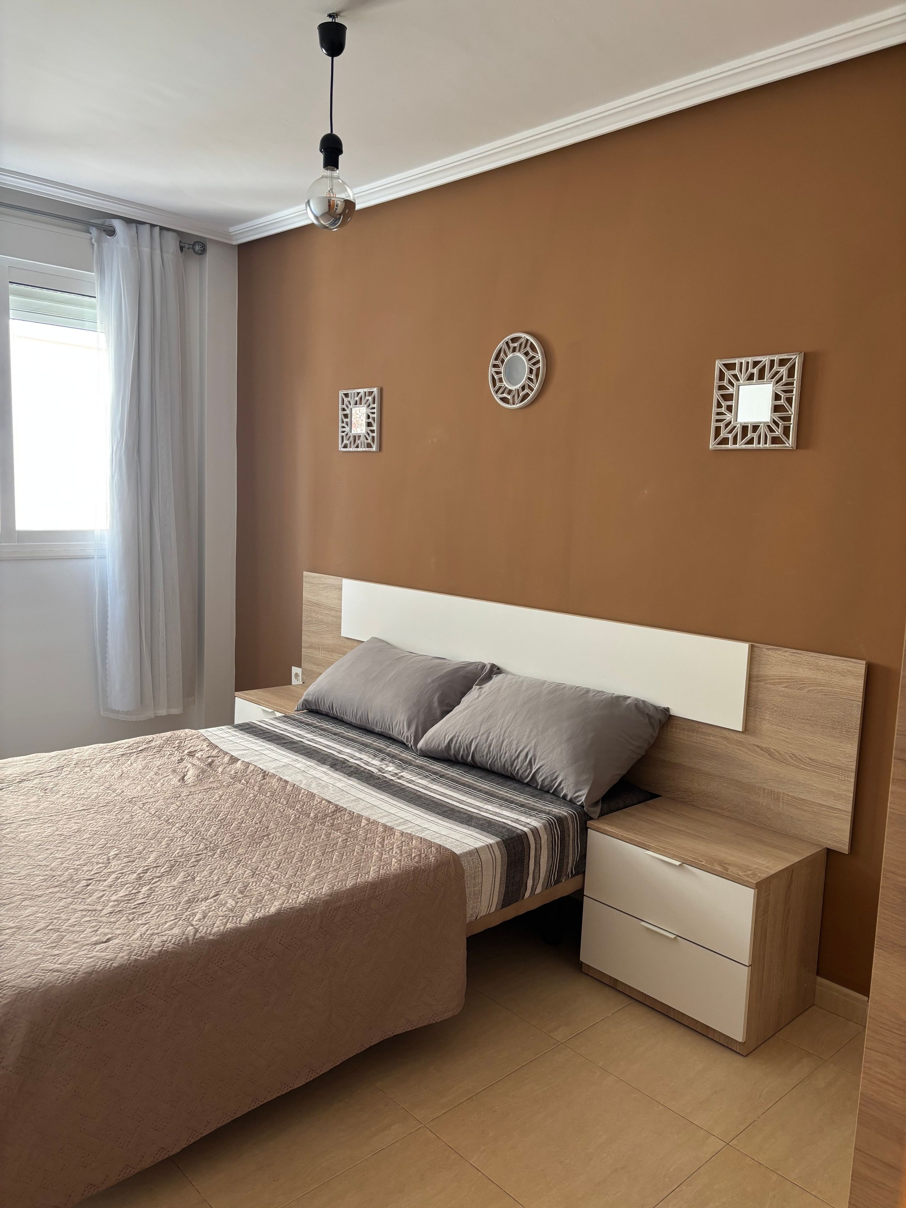 A bedroom with a large bed, bedside tables, a hanging light fixture, and decorative wall pieces.