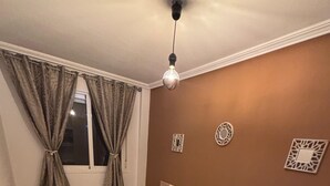 Et soveværelse med seng, natborde, gardiner, en loftlampe og dekorative billeder på væggen.