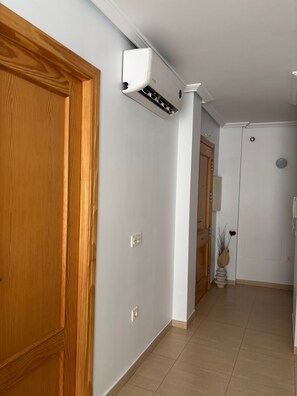 Un couloir avec une porte en bois, un mur blanc et un appareil de climatisation fixé au plafond.