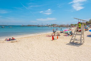A beach with a lifeguard tower, people sunbathing, and boats in the water.