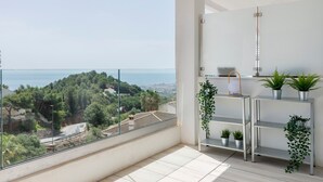 Un balcón con vistas despejadas al mar y la vegetación, un estante metálico con plantas y una pared blanca.