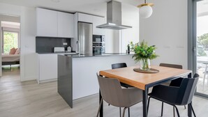 Una cocina moderna con una isla central, electrodomésticos de acero inoxidable y un comedor con mesa y sillas de madera.