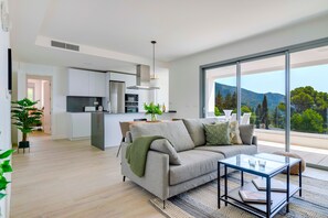 A modern living space with a sofa, coffee table, and a view of mountains through large windows.