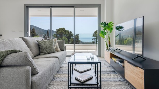 Una sala de estar moderna con sofá, mesa de centro, televisor y vistas al exterior.