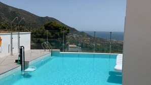 Una piscina azul cristalina con vistas al mar y colinas al fondo.