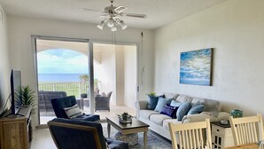 A living room with a sofa, armchair, dining table, and a balcony with a view of the ocean. - Oceanfront Condo, Private Balcony (Palm Coast)