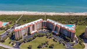 A multi-story hotel with a pool on the rooftop, surrounded by a parking area and greenery, overlooking a beach and the ocean. - Oceanfront Condo, Private Balcony (Palm Coast)