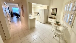 A modern kitchen with white cabinets, a refrigerator, and a dining area with a table and chairs. - Oceanfront Condo, Private Balcony (Palm Coast)