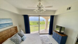 A bedroom with a bed, a TV, a ceiling fan, and a balcony with a view of the sea. - Oceanfront Condo, Private Balcony (Palm Coast)