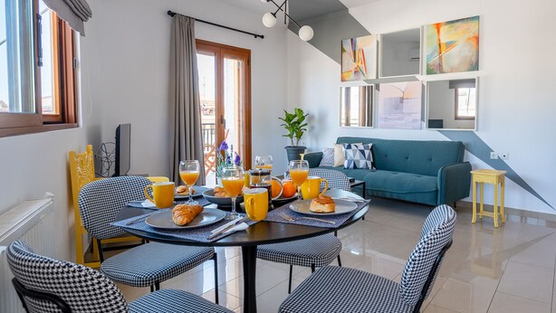 A dining area with a table set for breakfast, a sofa, and a potted plant. - Meros Filikon - Stylish Two Bedroom apt. (100m2) (Zakinthos)