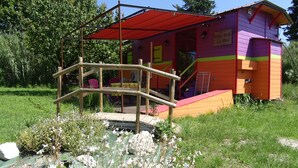 A colorful wooden structure with a red roof, surrounded by greenery and flowers.