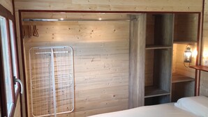 A wooden-paneled room with a bed, a metal rack, and a shelf unit.