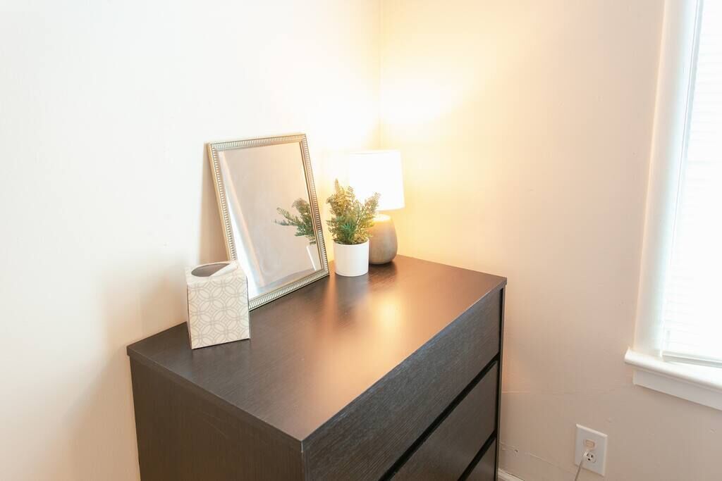 A dark wooden dresser with a framed mirror, a small potted plant, and a tissue box.