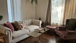 Un salon avec un canapé blanc, une table basse en verre, un fauteuil rose et une petite table sur laquelle se trouve un cactus.
