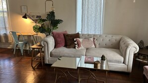 Un salon avec un canapé blanc, une table basse en verre, un bureau avec une chaise et une grande plante.