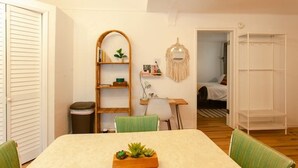 Una habitación acogedora con una mesa de comedor, sillas, una estantería, un tapiz de macramé y una cama al fondo.