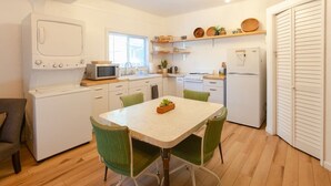 Una cocina compacta con electrodomésticos blancos, una mesa de comedor con sillas y una ventana que proporciona luz natural.