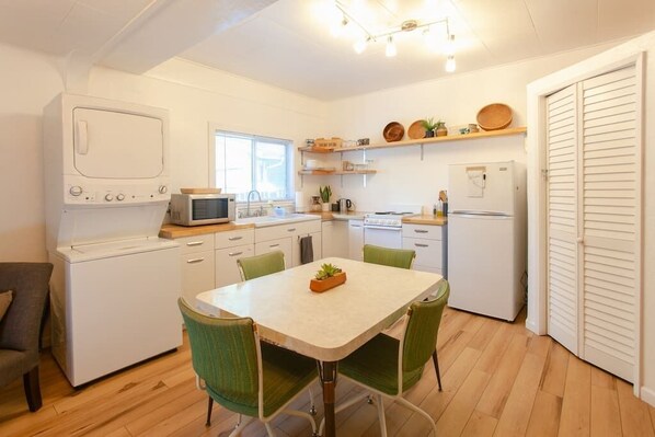 A compact kitchen with white appliances, a dining table with chairs, and a window providing natural light.