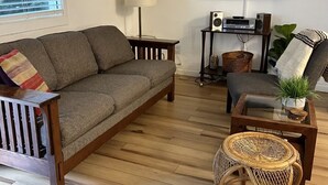 Una sala de estar con un sofá, una silla, una mesita, una lámpara, un televisor y un equipo de aire acondicionado.