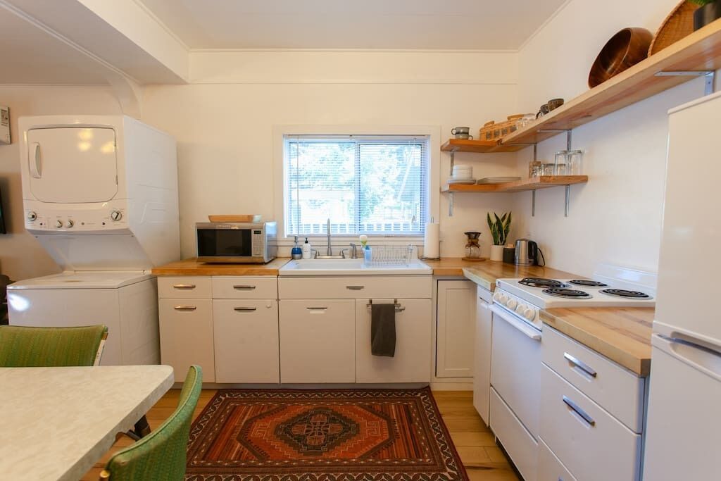 A compact kitchen with white cabinets, a microwave, a stove, and a window with blinds.