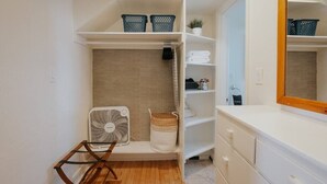 Une petite salle de bain avec un meuble-lavabo blanc, un miroir, un ventilateur et des étagères de rangement.