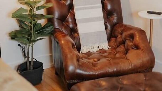 Un fauteuil en cuir marron, agrémenté d’un plaid rayé, d’une petite plante en pot et d’un lampadaire noir.