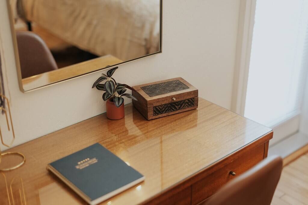 Un bureau en bois, un miroir, une plante en pot, une boîte décorative et un livre.