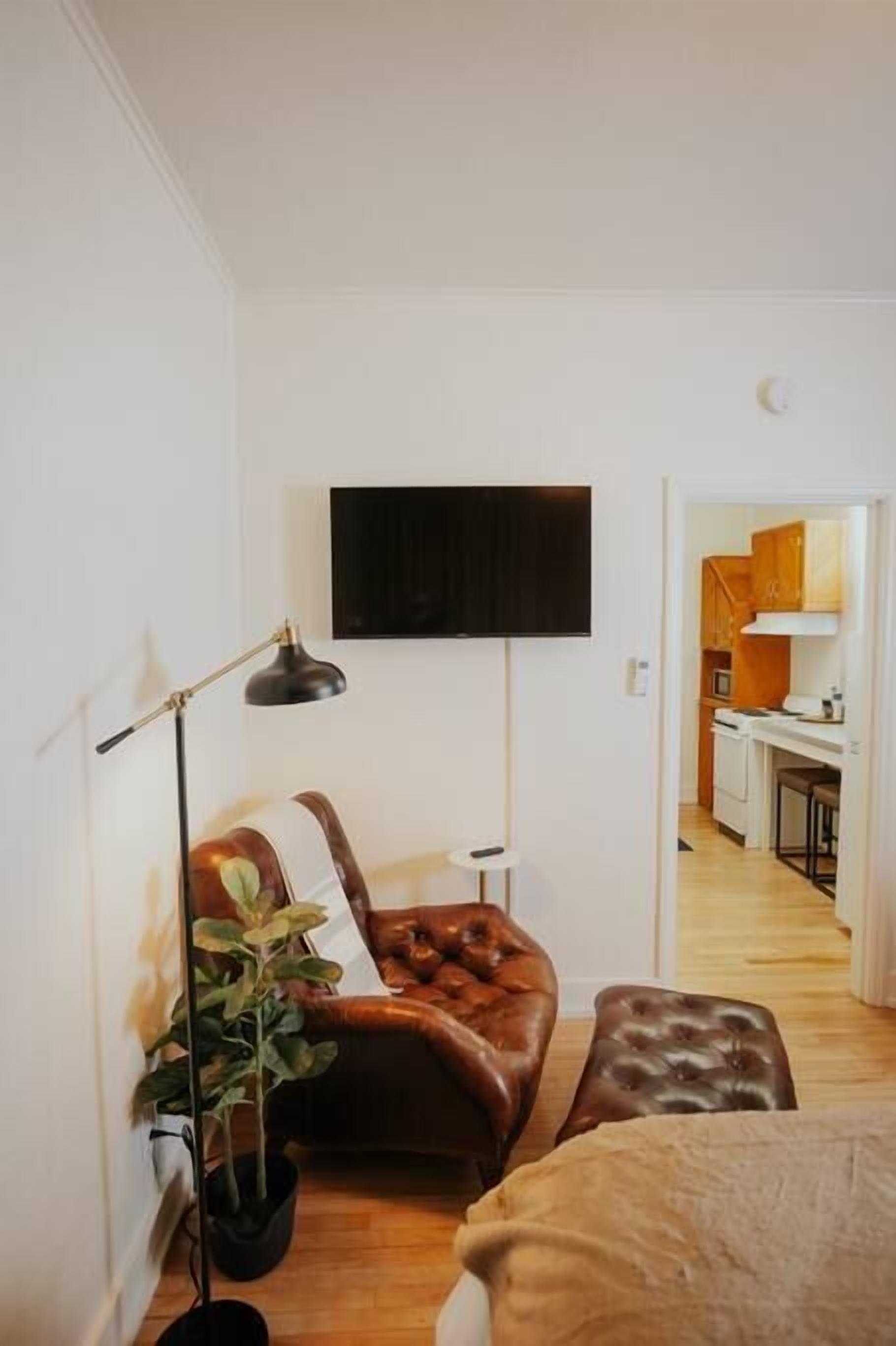 A compact living space with a sofa, a small table, a floor lamp, and a TV mounted on the wall.