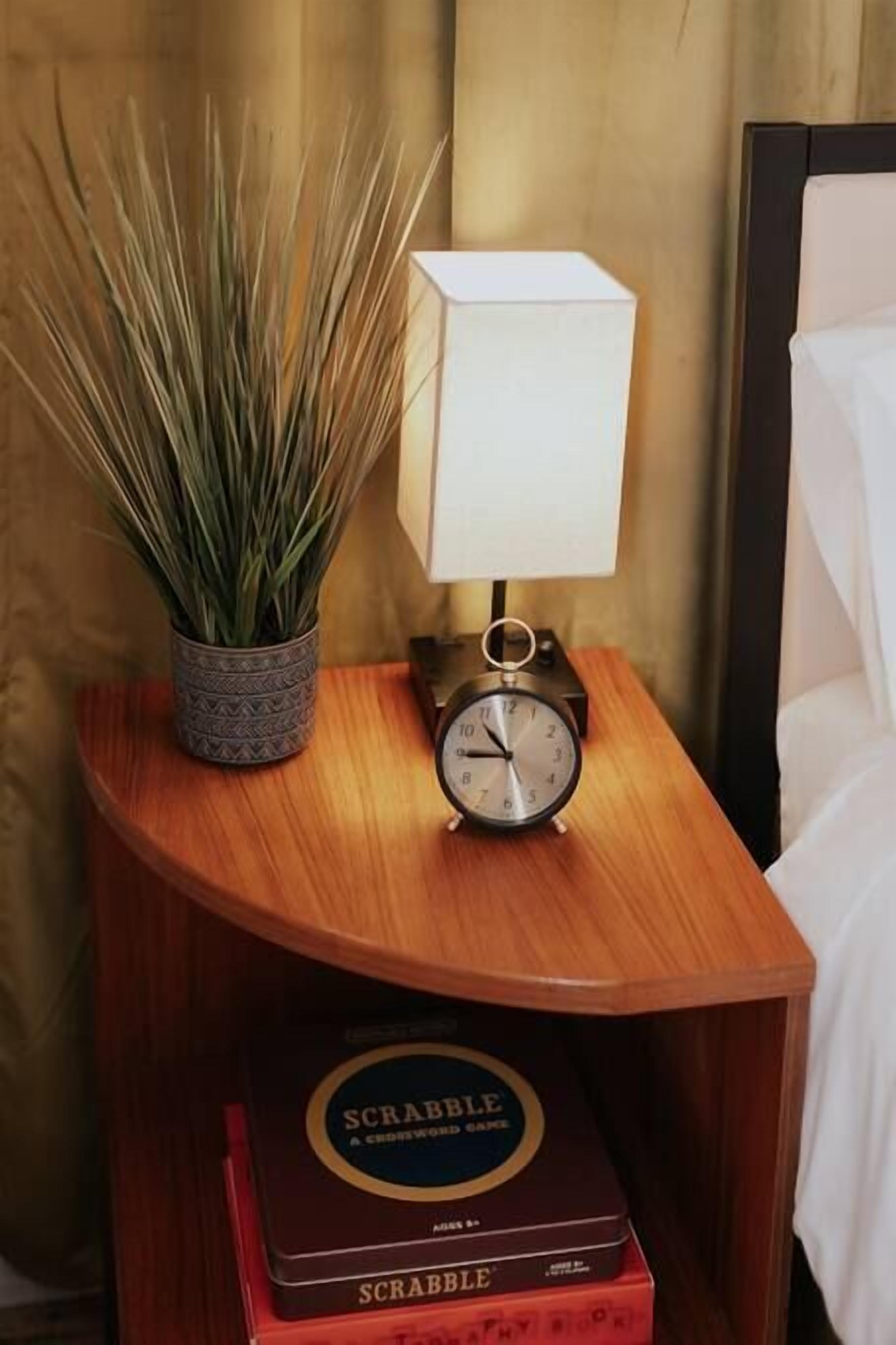Una mesita de noche con una lámpara, un reloj y dos cajas de Scrabble.