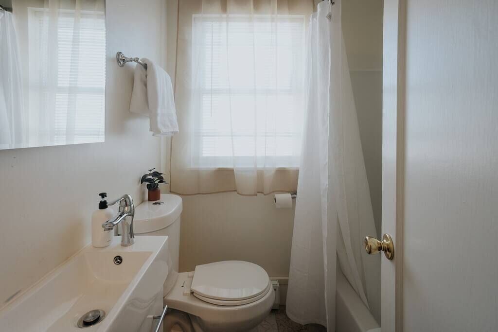A small, clean bathroom with a sink, toilet, and a window with curtains.