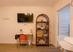 Una habitación con escritorio, silla, estantería, televisor y puerta.