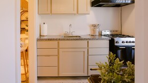 Une cuisine de taille réduite avec des meubles blancs, un évier en acier inoxydable et une cuisinière à gaz.