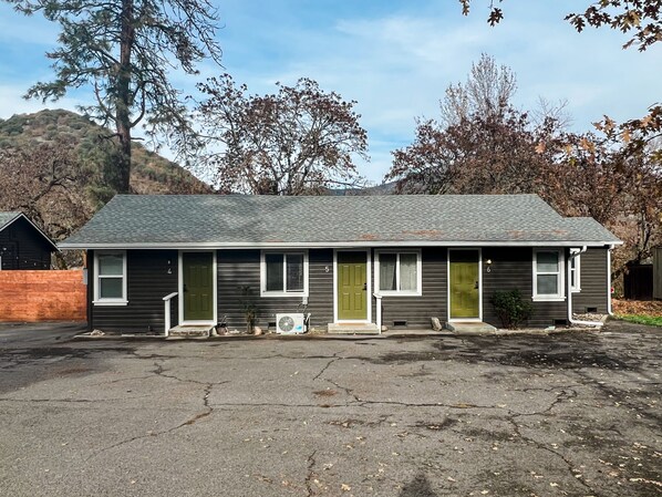 A single-story house with a grey roof and dark siding, numbered 5 and 6, with a driveway in front.