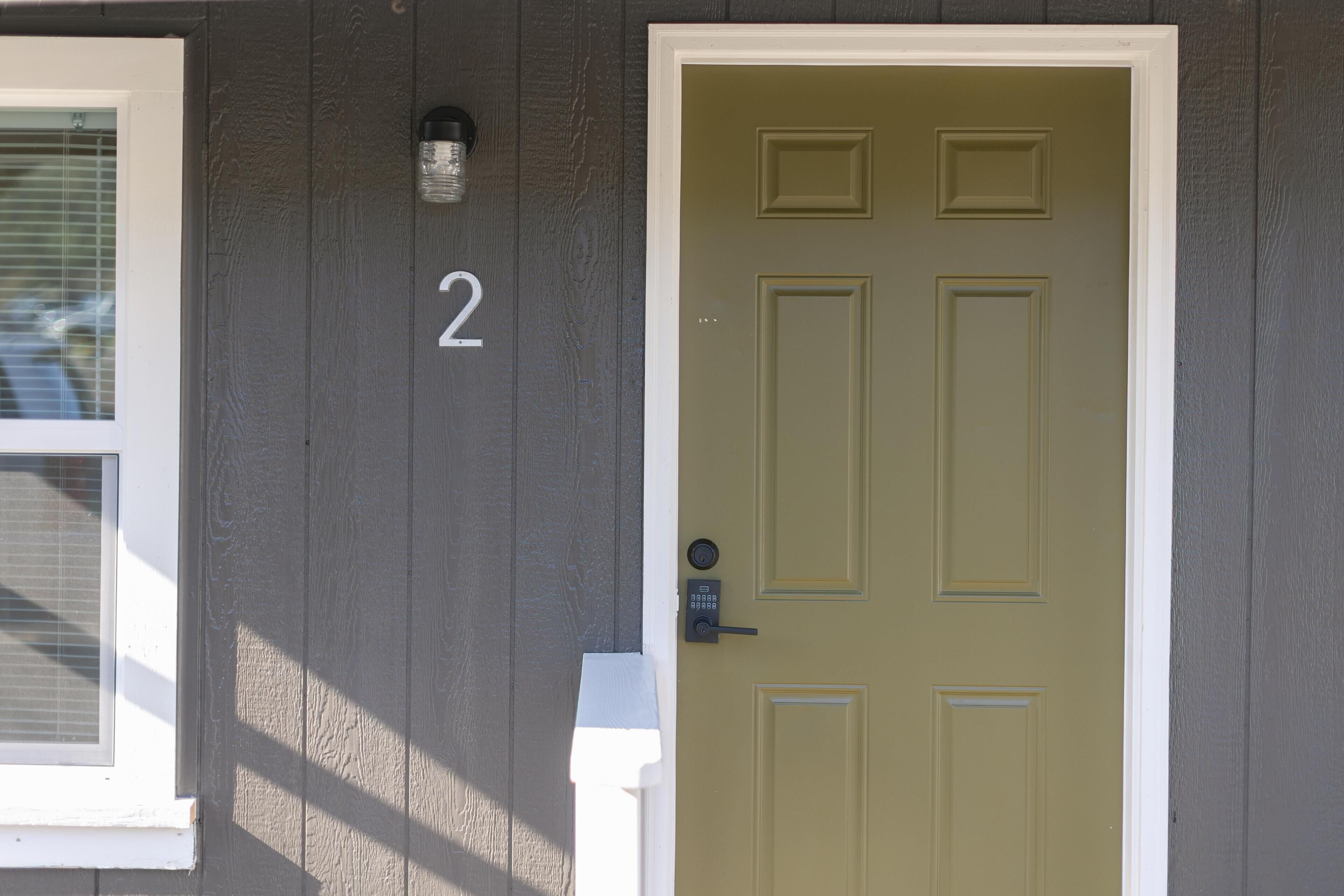 Une maison avec une porte verte, le chiffre « 2 » peint en blanc sur le mur, et une fenêtre avec des stores.