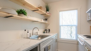 Una cocina moderna con encimeras de mármol blanco, electrodomésticos de acero inoxidable y estantes de madera.