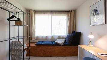 A compact room with a wooden bench, a desk, and a shelving unit with hangers and an ironing board.