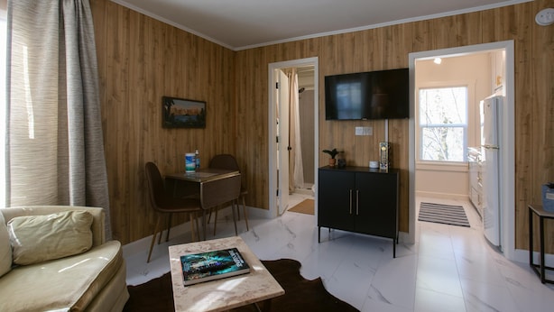 Una sala de estar con un sofá, una mesa de centro con un libro, un televisor y un comedor con una mesa y sillas.