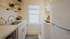 A compact kitchen with white cabinets, a stainless steel sink, and a window with sheer curtains. - Located in a scenic area perfect for travelers along I-5. You are right by the Rogue River, offering stunning views and tranquility, yet conveniently positioned for easy travel access. (Gold Hill)