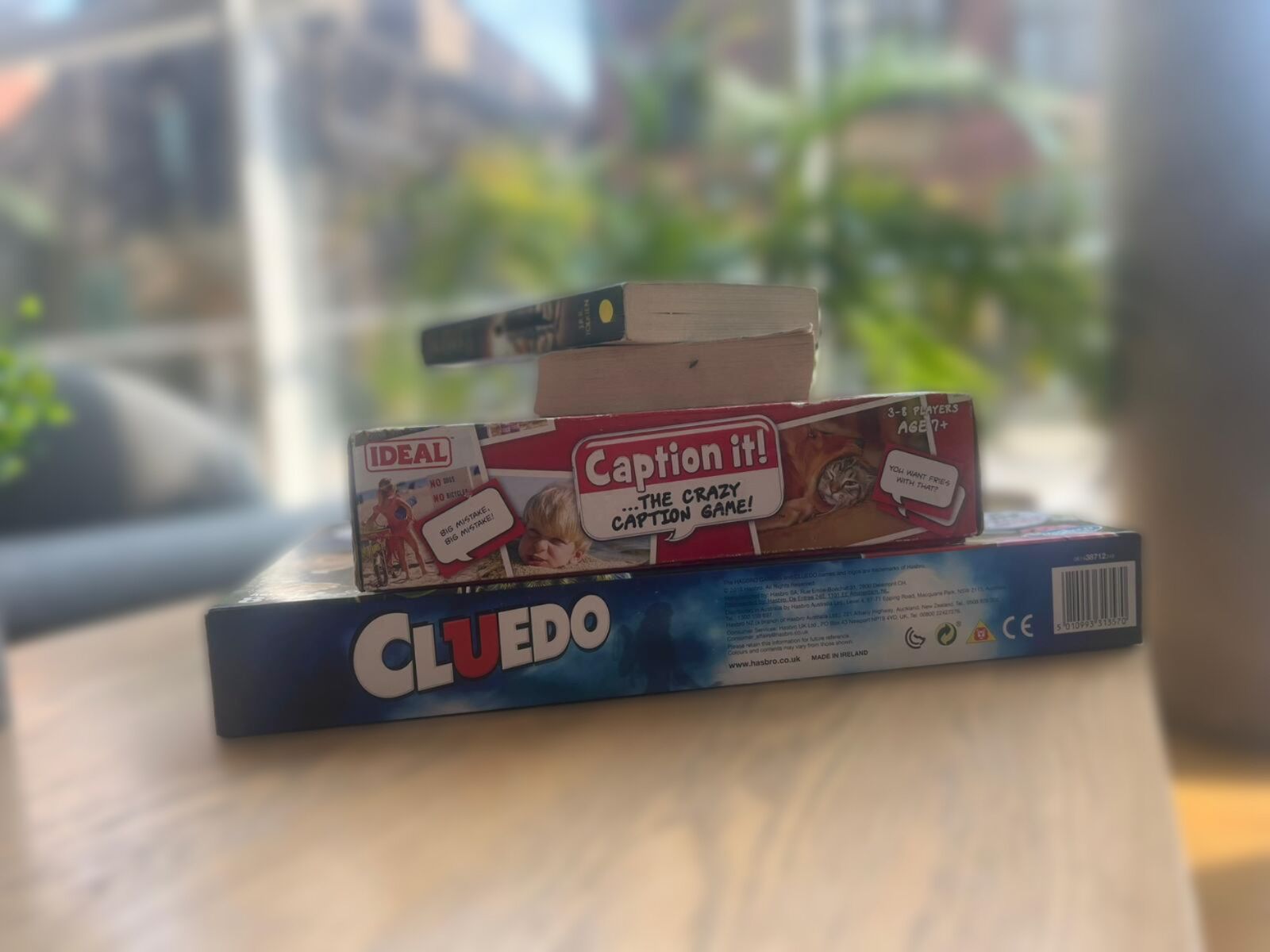 En spelkartong märkt med "Cluedo", med texterna "Ideal" och "Caption it!" på, placerad på ett bord.