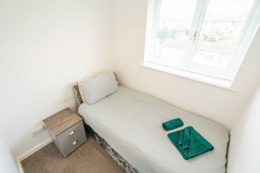 Une petite chambre avec un lit simple, une fenêtre, une table de chevet et une serviette enroulée posée sur le lit.