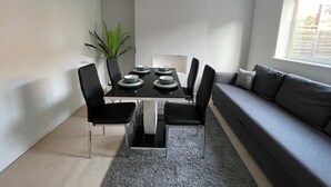 A modern living room with a dining table set for six, a grey sofa, a large window, and a potted plant. - Bright & Airy 3BR Home with Parking (Sheffield)