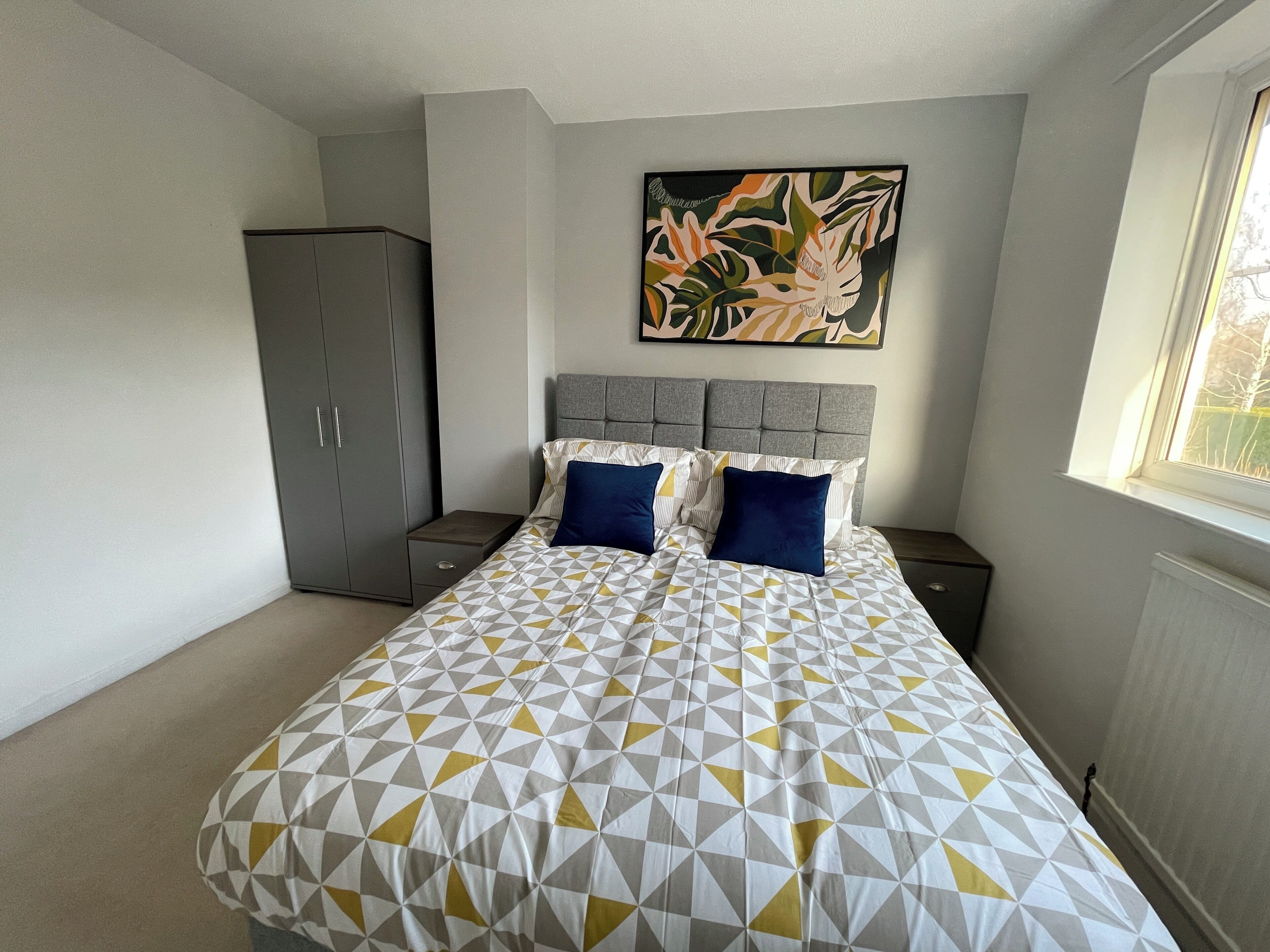 A bedroom with a bed, grey wardrobe, and a painting on the wall.